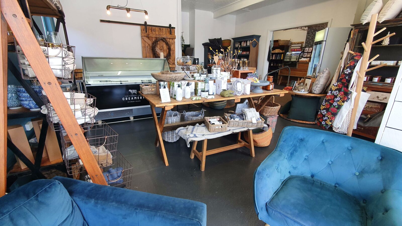 The interior of a shop, with white walls, blue chairs, a wooden table with colourful display