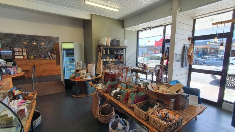 Interior of a shop, with white walls, a wooden table with a colourfil display, and windows