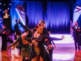 Two dancers peform latin dance on dance floor with adjudictors in the background
