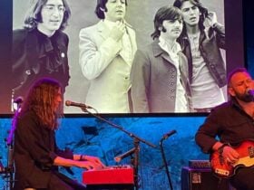 Two musicians sitting on stage, singing and playing instruments.