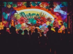 A crowd of people shot from behind enjoying a show from a brightly lit stage from the 2025 festival.