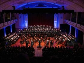 Choir and orchestra performing classical music to an audience in a concert hall.