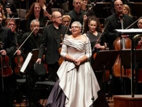 lady dressed in siver smiling on stage in front of an orchaestra