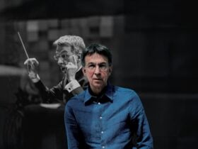 Eivind Aadland wearing glasses and a blue shirt stands in the foreground, facing the camera. Behind