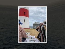 Two artists creating near a red and white lighthouse by the sea under cloudy skies.