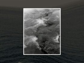 Black and white photo of ocean waves over rocks, with motion blur and a dark sea background.