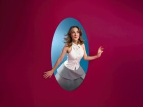 Woman in a white top peering through an oval cutout in a magenta wall into a blue space.