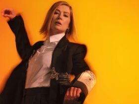 Rosamund Pike in front of a yellow background wearing a suit