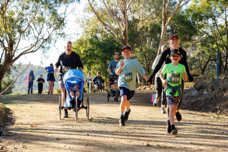 Young boys run with their parent while another runner runs with a child in a pram