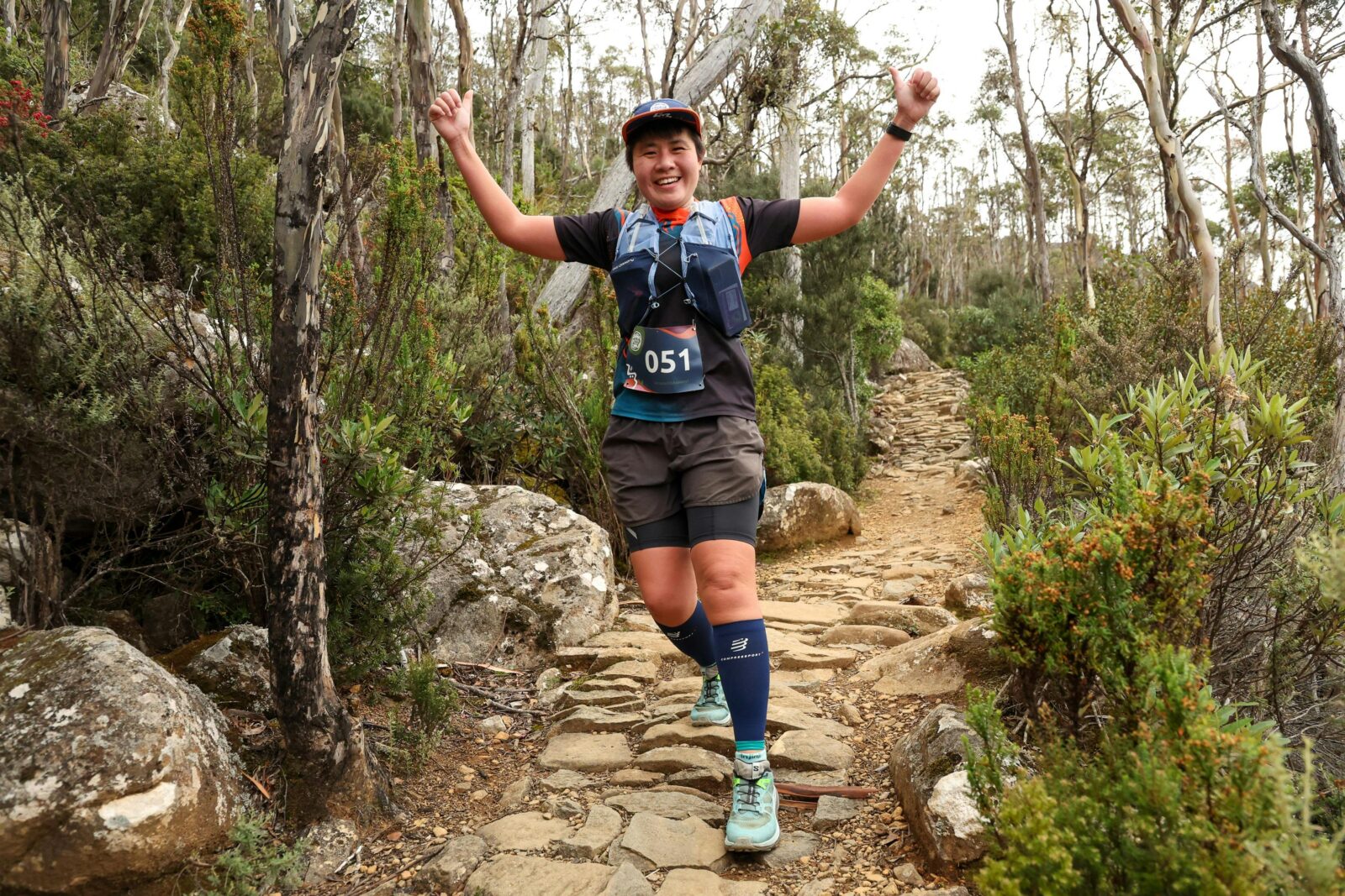 A female runner on the Organ Pipes Track with arms in the arm and a large smile