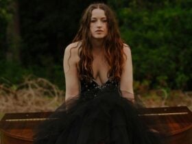 A woman wearing a black dress sits outdoors on a piano