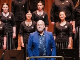 A medium shot of choral conductor David Squire standing in the foreground, wearing a vibrant blue su