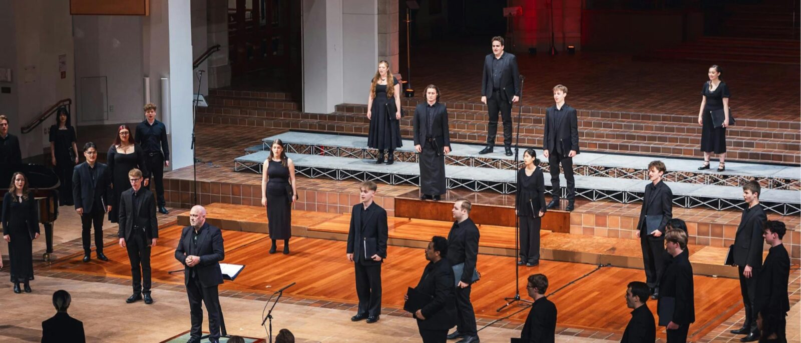 A group of singers dressed in black stand on a stage in front of microphones