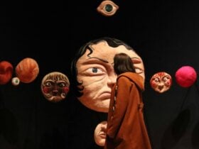 Woman standing in front of large scale needle felting faces by Tasmanian artist Frances Reeve Palmer