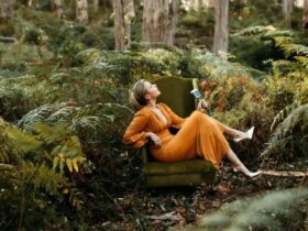 A woman wearing an orange dress holding a microphone sitting on an armchair in a forest