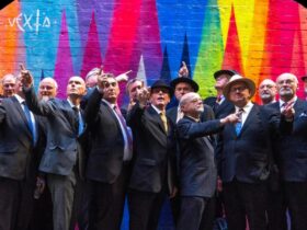 The singers of Men in Suits wearing business suits standing in front of a rainbow-coloured wall