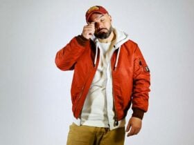 A man in orange jacket and hat with hand on face