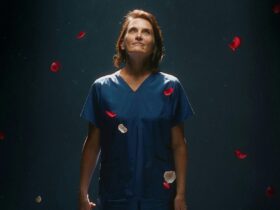 A middle aged woman wearing scrubs holds a bunch of rosed as petals fall from the sky.