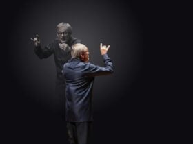 Conductor Simon Halsey is shown from behind with arms raised in a conducting gesture.