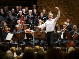 A conductor on stage before a group of choristers.
