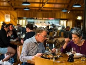 Couple eating a meal in Kauri Bistro with other patrons & Cape Grim Grill visible in background