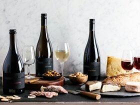 three bottles of wine placed alongside glassware, cheese, and meat items