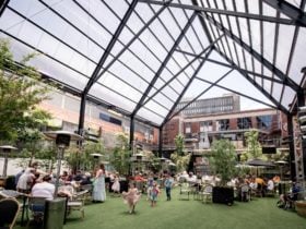 Families sit around tables and children play nearby, all under the 18 metre tall roof