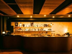 Warm-lit bar with curved counter, backlit shelves, and bottles on display.