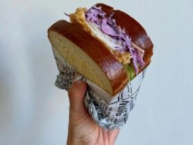 Crispy fried chicken sandwich with slaw on a soft bun, wrapped and held in hand.