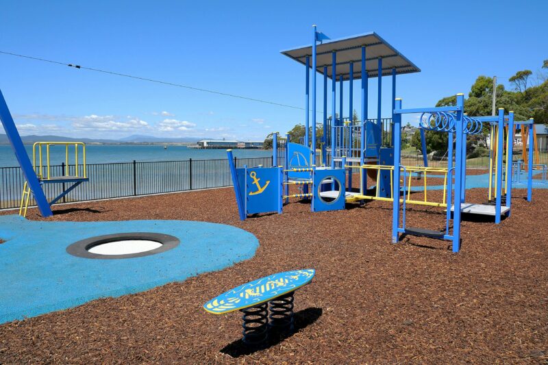 a range of playground equipment enclosed by railing fence, that sits alongside the water edges
