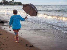 Colourful woman walking barefoot on Penguin Beach, TAS with an umbrella open, ready for seamist!