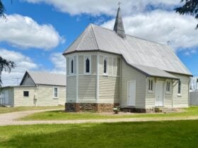 Country church in foreground with hall behind framed by trees