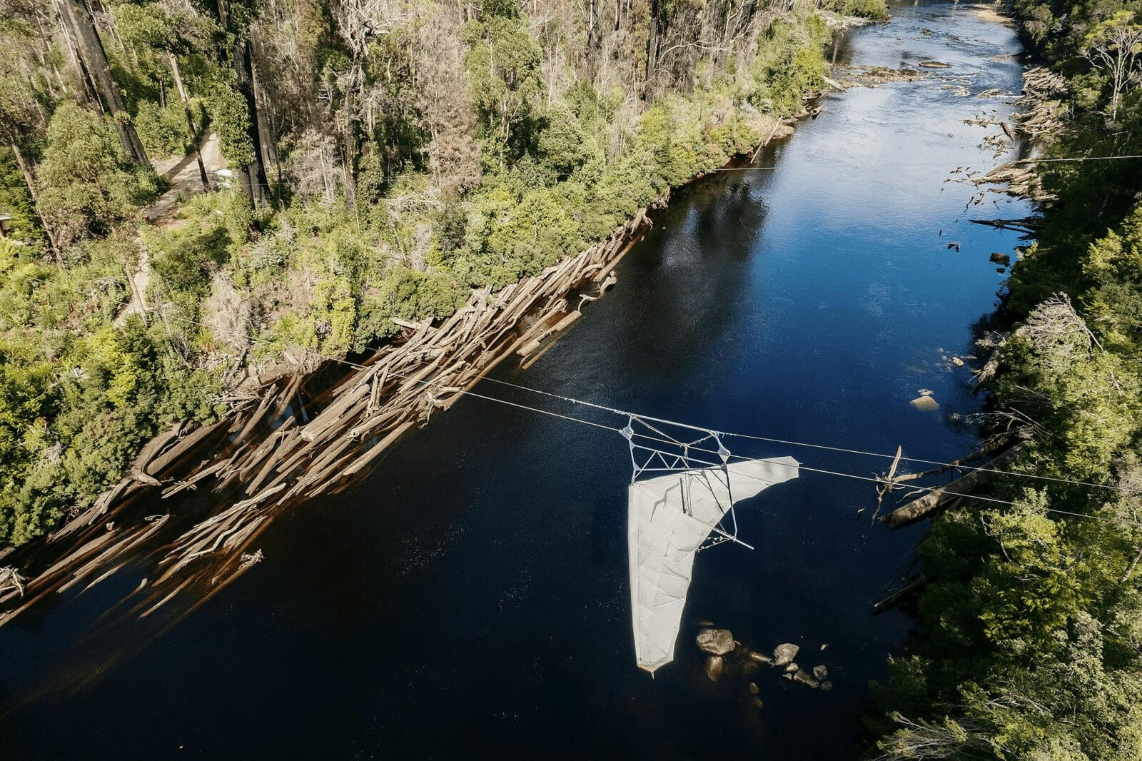 A bird's eye view of zipline with harness zooming across the river, with tall trees on either side