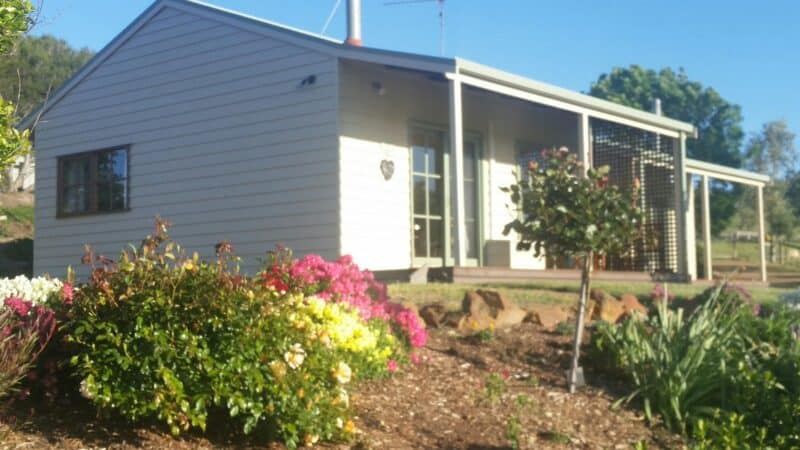 Cream and green weatherboard cottages sit in their own cottage garden in the side of a hill.