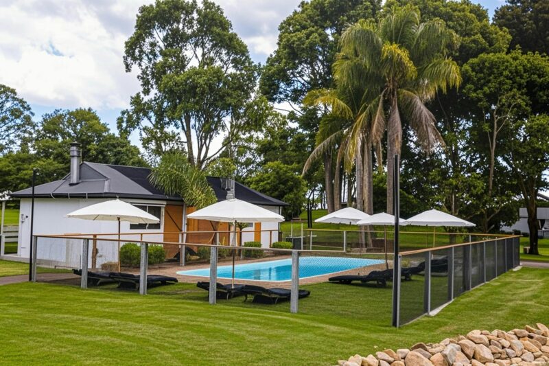 Solar heated pool at Eight Acres with sun loungers, umbrellas and palm trees and cottages