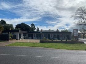 A full shot of the motel. A grey, newly painted building that is L shaped. Set on the main road.