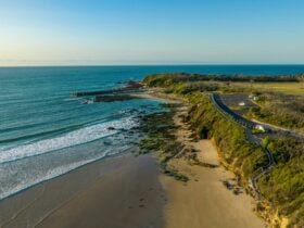View of the sea with carpark and walkway with stairs leading down to beach with waves breaking