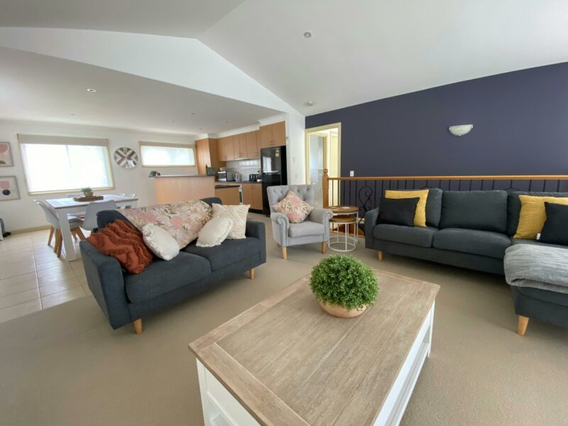 Image of living area looking towards kitchen, stairway balustrade visible behind couch