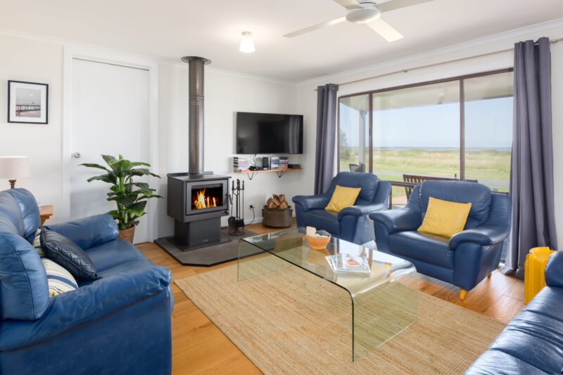 Living room with a 3 seater and 2 seater couches and 2 chairs with a Coonara wood heater.
