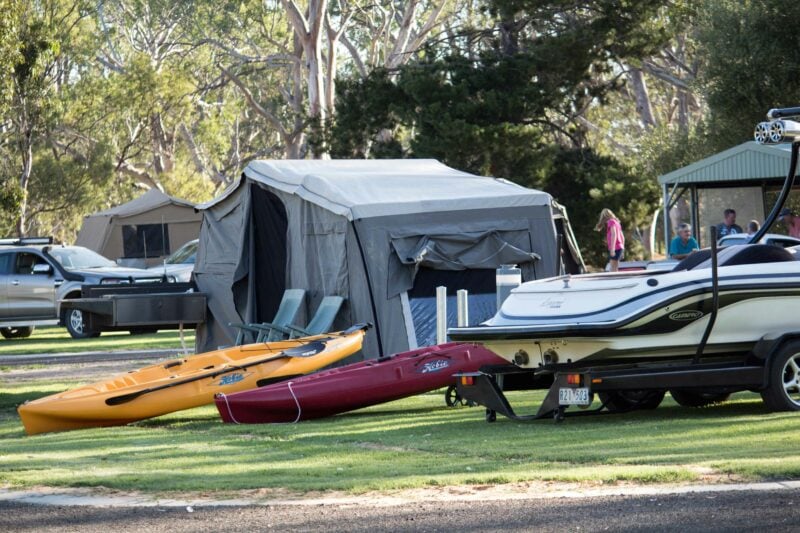 Tents, canoes, and ski boat, bushland trees in background