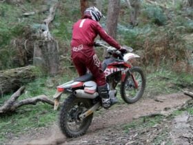 person in a red race suite with a helmet riding a dirt bike in the forest