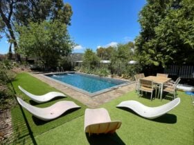 a Swimming pool surrounded by lounge chairs and a wooden dining table with dining chairs