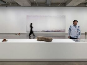 A photograph of two people looking closely at a large abstract painting and sculptural objects