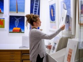 young woman looking at a print in fornt of blue colourful paintings