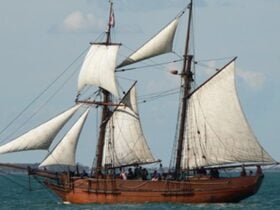 A small tall ship sailing with six sails set and people on deck