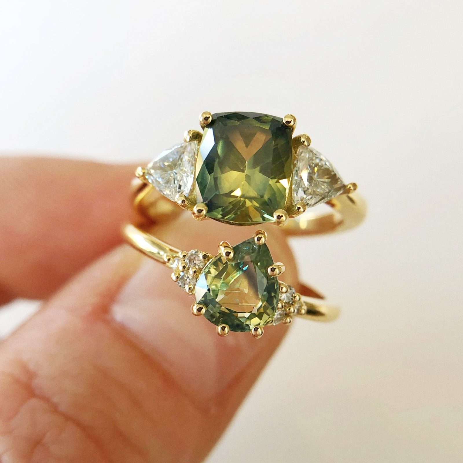 Two Sapphire and Diamond Yellow Gold Rings held against a pale cream background