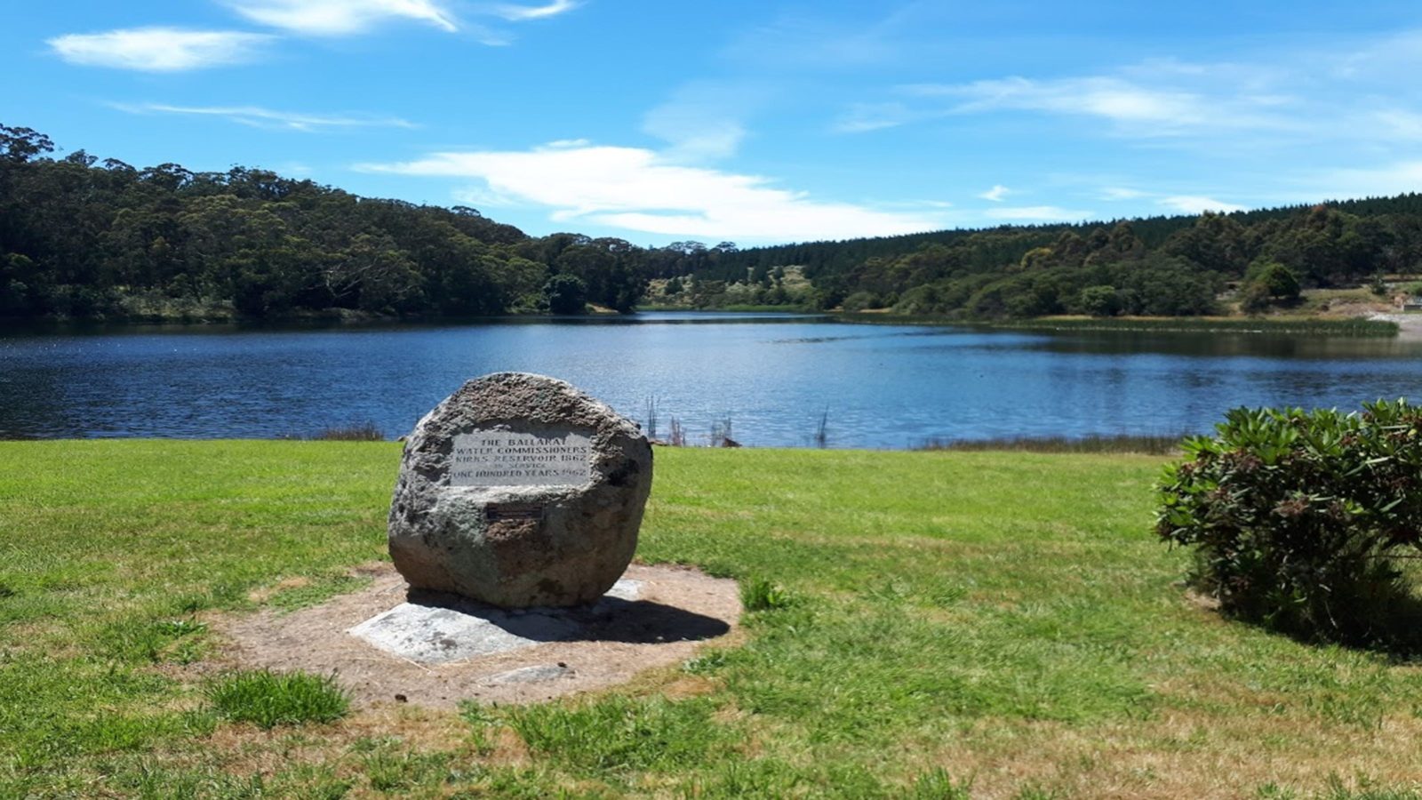 reservoir with trees in background with blue skies overhead and plague on rock in foreground
