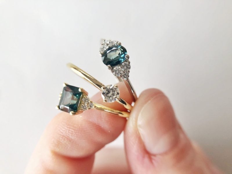 A close up photo of three fine rings held between the thumb and forefinger.