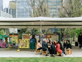 A group sits in front of a display of artworks at MPavilion Parkville.