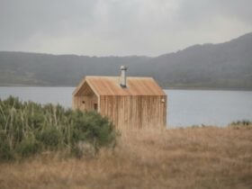 Nature shot of light coloured wood sauna with chimney on lake in the mountains